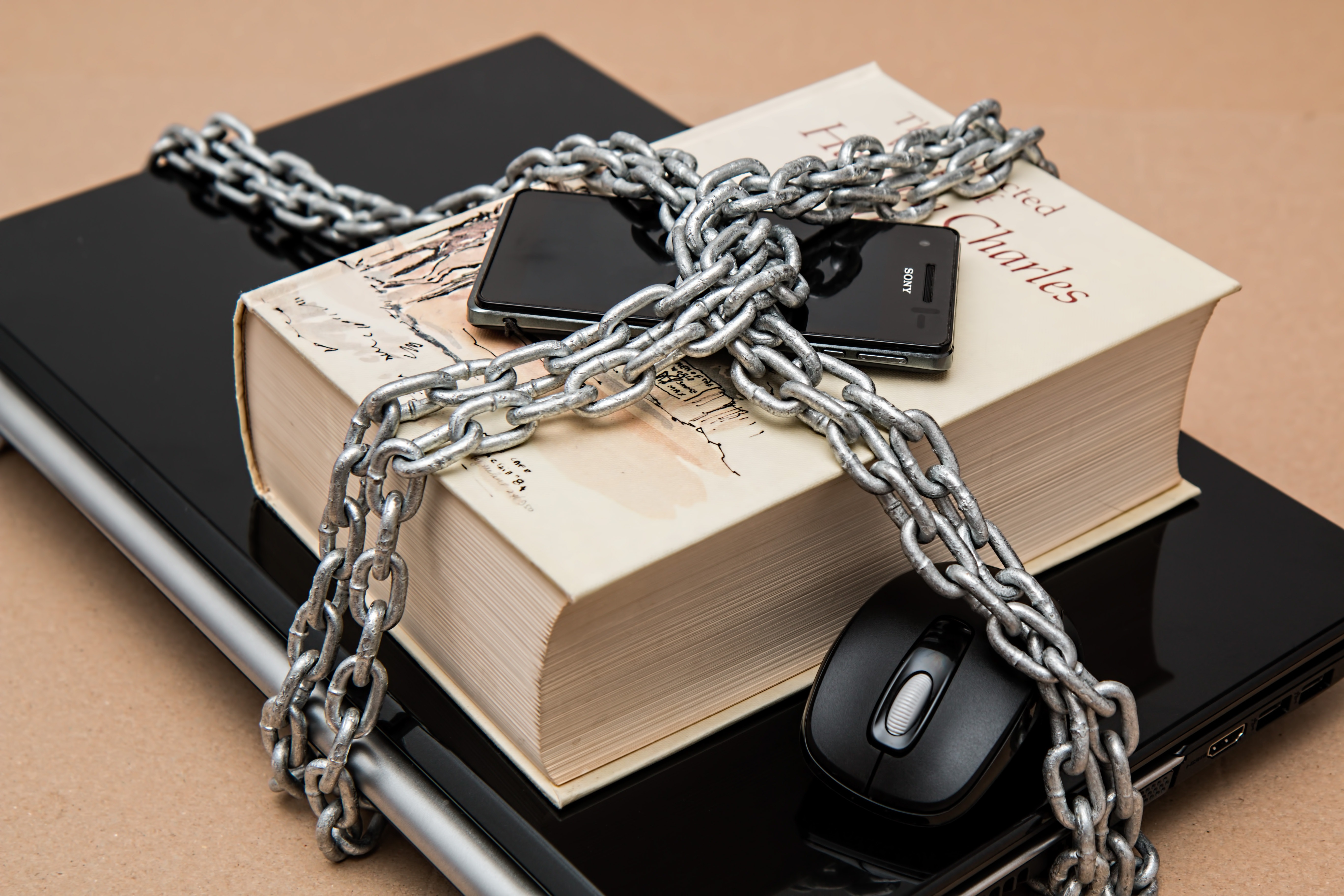 Laptop phone and book wrapped in chains